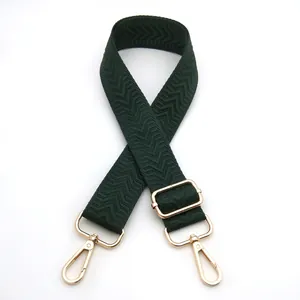 Detail of dark green woven bag strap with golden metal hooks and chevron pattern texture