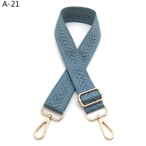 Detail view of grey-blue chevron woven bag strap with adjustable gold buckle and swivel hooks
