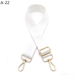 Close-up of white chevron woven shoulder strap with gold metal lobster clasps and buckle