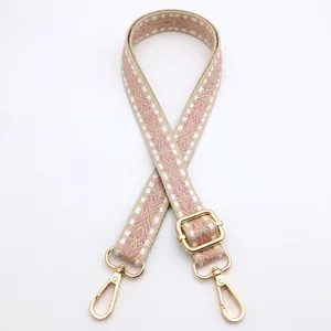 Detail view of pink and beige geometric woven bag strap with golden lobster clasps