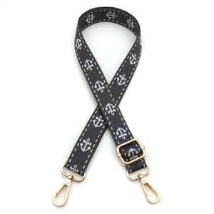 Close-up of black adjustable bag strap with white anchor embroidery and gold metal hooks