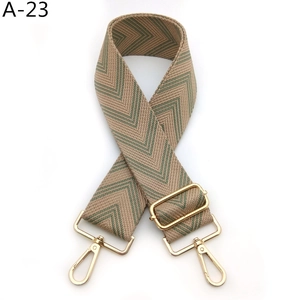 Detail of adjustable beige and green herringbone pattern bag strap with gold metal hooks
