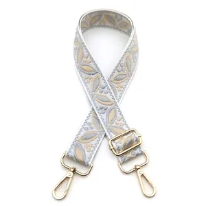 Detail of adjustable wide guitar style bag strap with floral embroidery and gold hooks