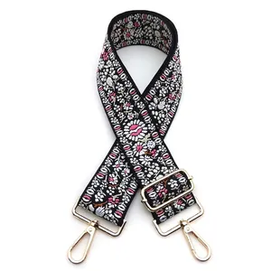 Close-up of ethnic floral embroidery on a wide black bag strap with gold metal buckles