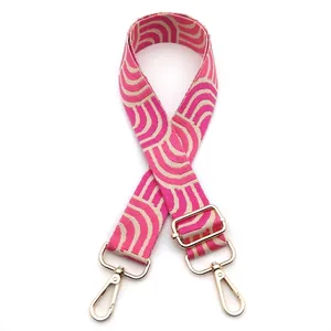 Detail of adjustable woven bag strap with pink geometric waves and gold metal hooks