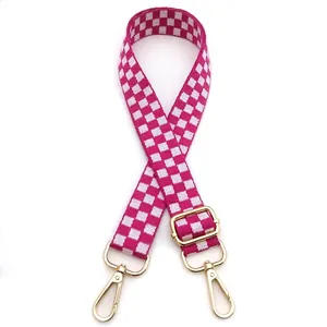 Detail view of pink checkerboard woven strap with golden metal hardware and swivel hooks