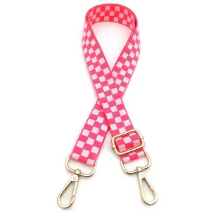 Close-up of pink and white checkered bag strap with gold metal lobster clasps and buckle