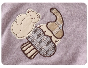 Detail of cute teddy bear embroidery patch on purple knit baby bodysuit fabric