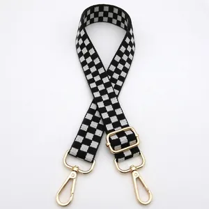 Close-up of black and white checkerboard bag strap with adjustable gold metal buckles