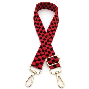 Detail of red and black checkerboard adjustable fabric bag strap with gold metal hooks