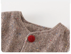 Detail of baby boy winter tweed vest showing brown herringbone fabric and red pompom button