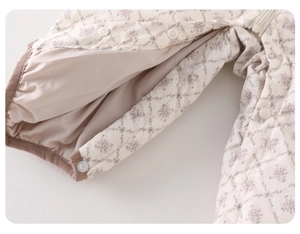 Close-up of quilted floral infant romper detailing white plastic snaps and soft lining