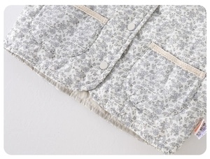 Detail of floral baby quilted vest featuring blue patterns and lace-trimmed pockets