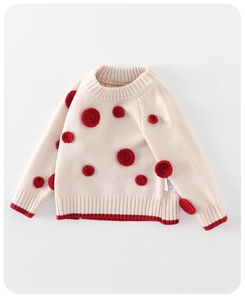 Close-up of baby winter knit sweater showing cream texture and red floral embroidery dots