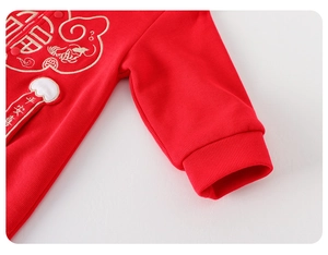 Détail d'un body de bébé rouge avec broderies dorées et motifs traditionnels