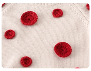 Detailed close-up of beige knitted sweater with handmade red crochet polka dots