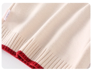 Macro detail of toddler cream knit sweater showing red ribbed hem and product care label