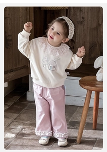 Detailed embroidery of house and trees on a beige sweatshirt with floral ruffle collar