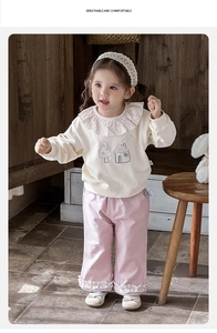 Detail of baby girl floral ruffle collar sweatshirt and pink wide-leg pants on wooden chair