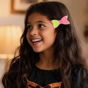 Sparkly pink and neon green sequin bow hair clip worn by a young girl with long dark hair