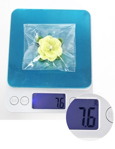 Macro view of handmade plush flower hair clip with pearl center on digital scale showing 7.6g