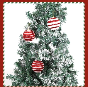 Detail of red and white striped glitter Christmas ornaments hanging on a snowy tree