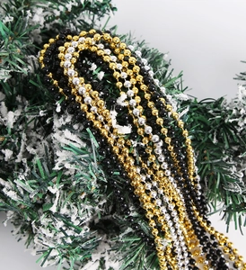 Detail view of gold, silver, and black bead necklaces on snowy Christmas branches