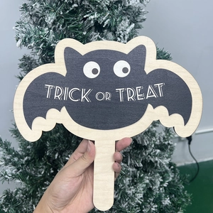 Halloween wooden bat prop with Trick or Treat text held in front of a festive tree