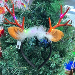 Christmas LED reindeer antler headband with red festive decor on pine tree branch