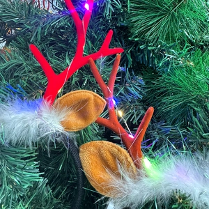 Detail of LED Christmas reindeer antler headband with festive feathers on green pine branches