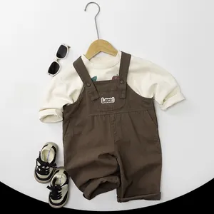 Detailed view of kids' brown overalls with embroidered Luck patch and beige long sleeve shirt