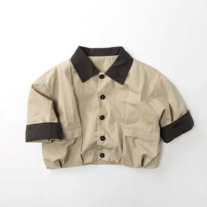 Detail of a beige neutral cotton jacket for kids with brown trim and large front pockets