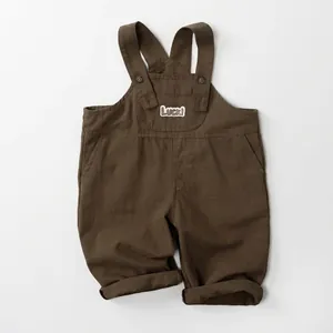 Detail of dark brown cotton-linen overalls with Luck! embroidery and adjustable straps