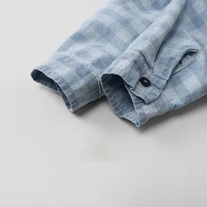 Close-up of blue and white checkered shirt cuff with black button and neat stitching