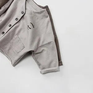 Detail of grey knitted kids cardigan featuring smiling face embroidery and single pocket