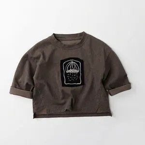 Detail view of cotton kids long sleeve tee with roll-edge hem and artistic chest patch