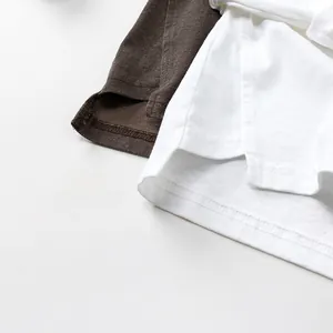 Close-up of side slits and double-stitched hem on cotton kids' t-shirts in brown and white