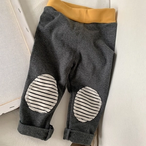 Detail of dark grey kids' leggings featuring yellow elastic waist and striped knee patches