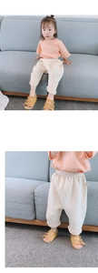 Détail d'une tenue d'été enfant avec t-shirt orange clair et pantalon sarouel blanc cassé