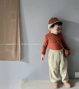 Detail of child wearing brick red thermal long sleeve shirt and beige corduroy trousers