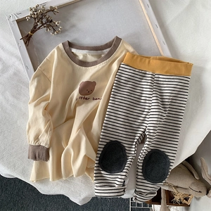 Flat lay of cotton infant set with yellow bear top and striped pants in a warm setting