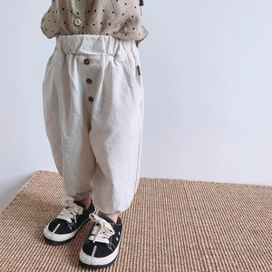 Detail of loose-fit beige kids casual trousers with elastic waist and button accents
