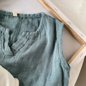 Dettaglio di un gilet traspirante in cotone e lino per bambini con scollo a V e trama blu morandi