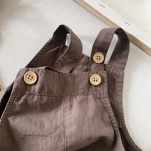Detail of brown cotton overalls featuring rustic wood texture buttons and soft fabric