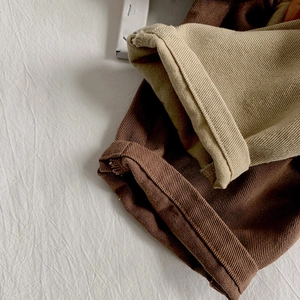 Detail of corduroy pants showing neat hem stitching and texture in brown and beige