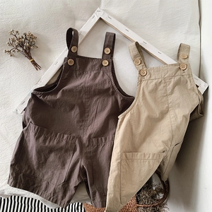 Detail of cotton kids overalls featuring wooden buttons and large patch pockets in earth tones