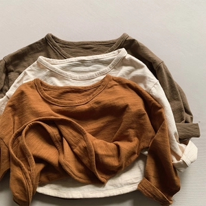 Texture detail of three slub cotton long sleeve shirts in olive, cream, and burnt orange