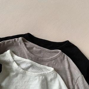 Detail of three slub cotton kids' t-shirts in black, grey, and cream with neck binding