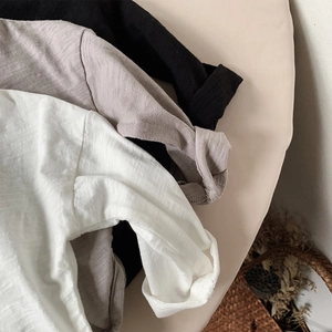Detail view of stacked long-sleeve cotton T-shirts in white, grey-purple, and black colors