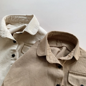 Close-up of beige and khaki kids' cotton shirts featuring black buttons and chest pockets